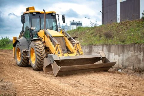 A tractor or a loader is parked on a dirt road, surrounded by fields and gree Stock-Fotos