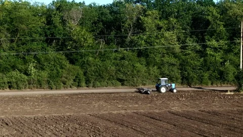 A tractor with a plow drives along the edge of the field, between the field and Stock Footage 143598884