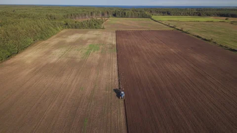 Tractor Plowing with Birds Amid Fields and Woodland with Distant Water Stock Footage 348437728