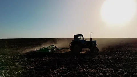 Tractor plowing field under bright sun, creating dust clouds as it moves Stock Footage 336066195