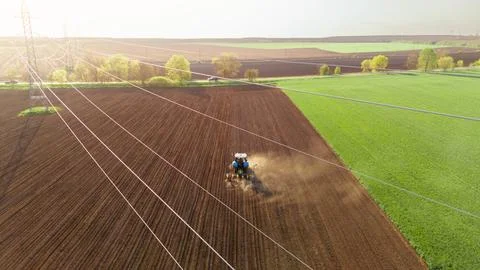 Tractor plows field in the spring. Aerial top view, power line in the foreground Stock Photos