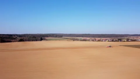 Tractor plows fields on a hill near forest and village Stock Footage 172379193