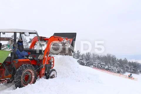 The tractor pours snow with his bucket on the ski slope. The work of the snow Stock Photos