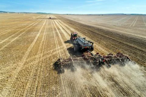 Tractor pulling an air seeder, seeding a field with blue sky in the distance Stock Photos