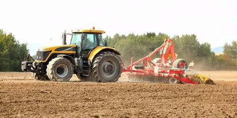 Tractor pulling ploughing / sowing trailer over dry field. Stock Photos