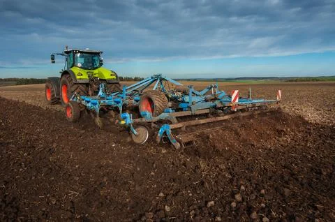 Tractor pulling a plow for sowing, beautiful sky with clouds above 스톡 사진