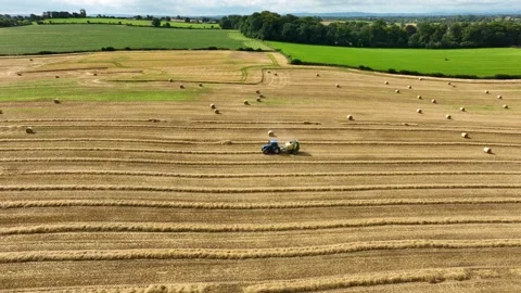 Tractor Pulling Round Baler Across Wide Countryside Field Dotted With Hay Bales Stock Footage 341470441