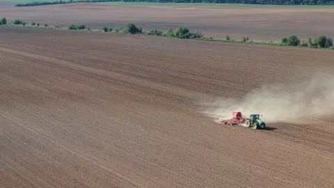 A tractor pulls agricultural machinery across a wide dry field, raising a large Stock Footage 317684772