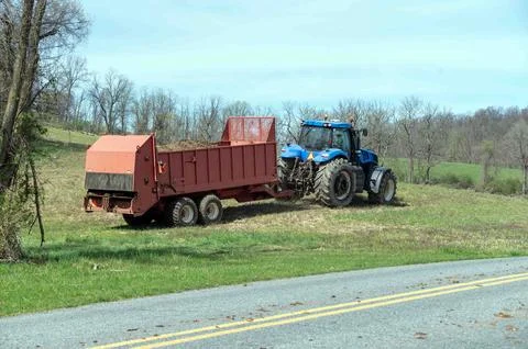 Tractor pulls red fertilizer manure spreader over agricultural field Stock Photos