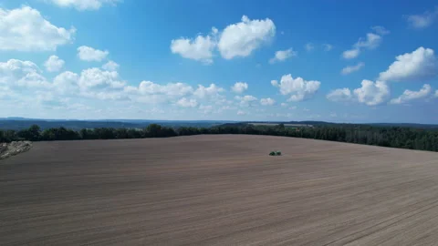 A tractor rides across a field spraying a sown field near a forest against a Stock Footage 197111569