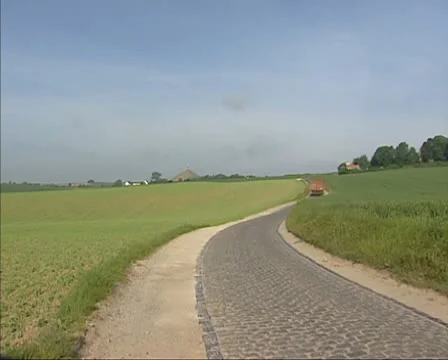 Tractor rides off camera on cobbled windy road in rural landscape Stock Footage 22000860
