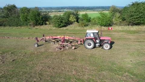 A tractor with a rotary rake rakes hay on agricultural land. Aerial video Stock Footage 167526302