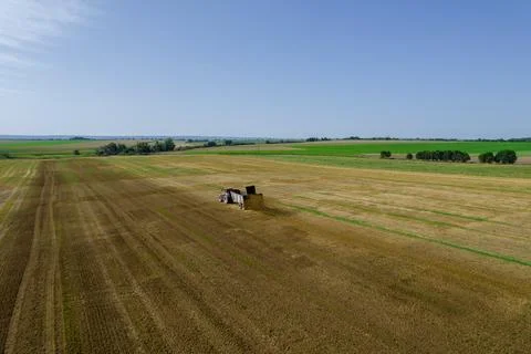 A tractor is scattering manure over a large field from a trailer nearby Stock Photos