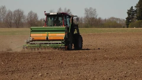 Tractor with seed drill working across a plowed farm field, raising dust while Stock Footage 334578833