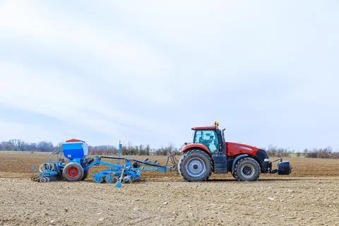 A tractor with a seeder in the field sows a large farmer's plantation with gr Stock Photos