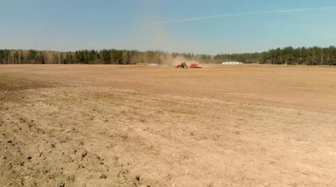 Tractor with a seeder is gathering dust on spring farmland 스톡 사진