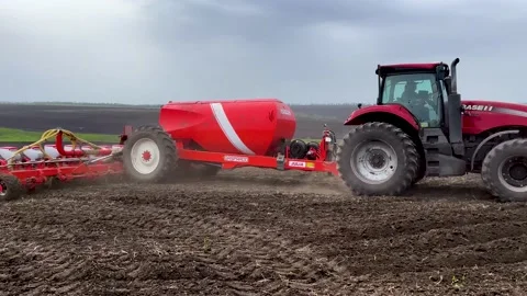 A tractor with a seeder rides through a black plowed field in the spring and Video stock 239175117