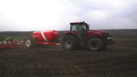 A tractor with a seeder rides through a black plowed field in the spring and Stock Footage 239313983