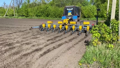 A tractor with a seeder rides through a plowed field with a planter and sows Stock Footage 240758928