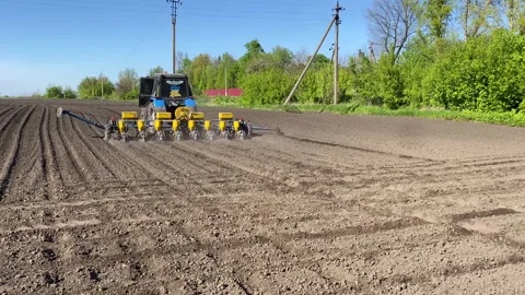 A tractor with a seeder rides through a plowed field with a planter and sows Stock Footage 241029071