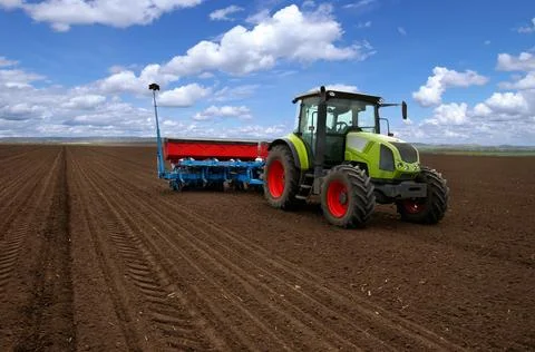 A tractor that sows crops with a seeder at arable field, beautiful sky Stock Photos