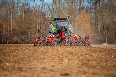 Tractor Towing Red Seed Drill on Early Spring Farmland at Daylight Stock Photos