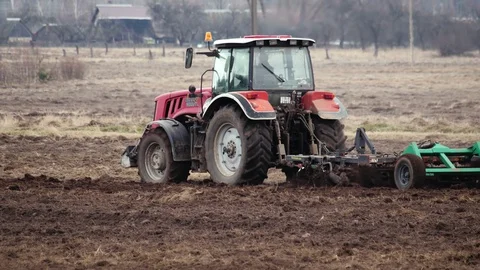 Tractor with a trailed disc harrow handles the field, village houses in the Video stock 128067776