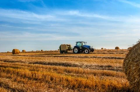 A tractor uses a trailed bale machine to collect straw in the field and make  Stock Photos