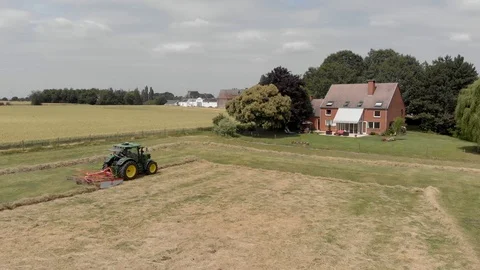 Tractor windrowing a field in a village Stock Footage 112985029