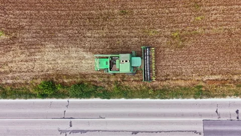 Tractor working in field next to road during daytime in a rural area Stock Footage 345454487