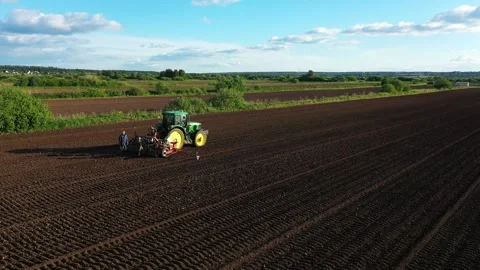 Tractor works on arable, lays rows for planting potato. Workers control process Stock Footage 246063030