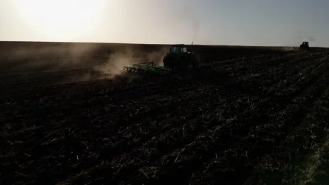 Tractors plowing a field under the sun, creating dust clouds while preparing the Stockbeeldmateriaal 336070084