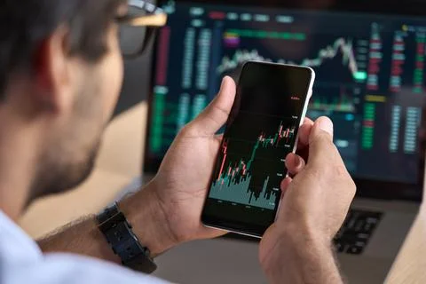 Trader broker using phone analyzing stock market trading charts data using app. Stock Photos