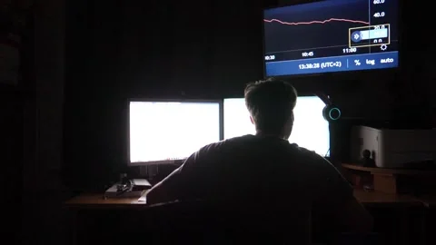 Trader focused on cryptocurrency analysis, seated at a desk with dual monitors Stockbeeldmateriaal 347870693
