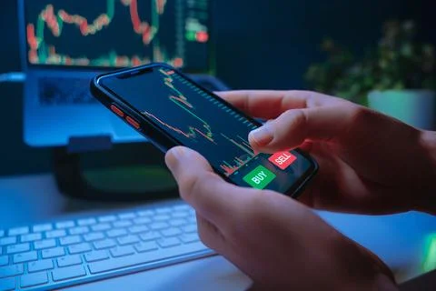 Trader hands using mobile trading app at night, buying crypto or stocks Stock Photos