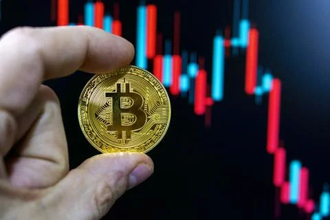 Trader holding bitcoin in front of candlestick chart showing price falling Stock Photos