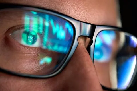 Trader looking at computer screen analyzing trading chart reflecting in glasses. Stockfoto's
