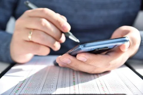 Trader man with pen in hand using smart phone with stock statistic Stock Photos