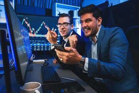 Traders comparing dynamic investment graph via phone and pc. Sellable. Stock Photos