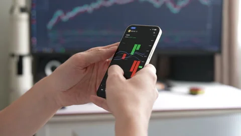 Trading professional analyzing financial graphs on smartphone screen, displaying Stock Footage 297631820