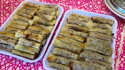 Traditional crispy meat spring rolls arranged in trays on patterned tablecloth Stock Footage 329591191