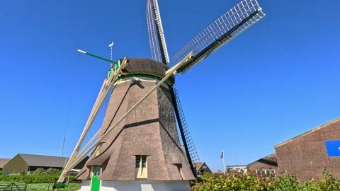 Traditional Dutch windmill with rotating sails against a clear blue summer sk Stock Footage 340229564
