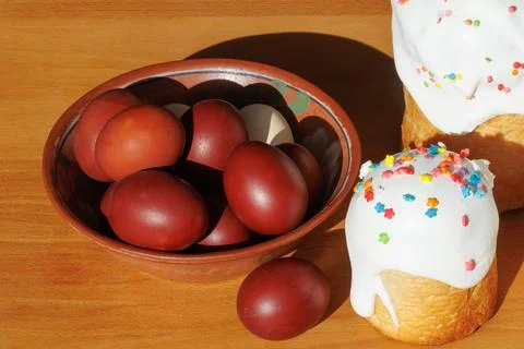 Traditional Easter red eggs in a clay bowl with festive glazed cake Stock Photos