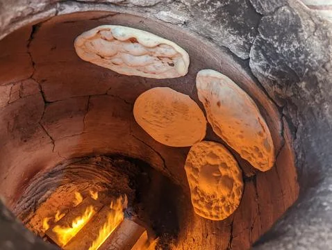 Traditional flatbreads baking in clay oven with glowing embers Stock Photos
