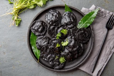 Traditional Italian black ravioli on black plate, gray stone slate background Stock Photos