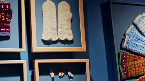 Traditional knitted mittens displayed in frames on a blue museum wall Stock Footage 332431138