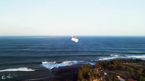 Traditional Long Tail Kite Gliding Above Rolling Ocean Waves and Rugged Dark Stock Footage 343462482