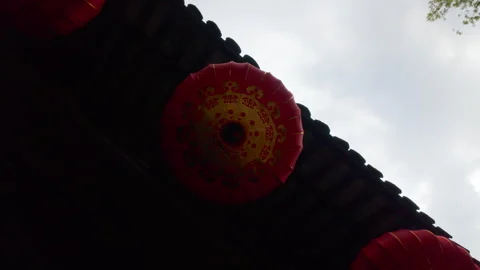 Traditional Red Lanterns Hanging Beneath Tiled Roof Against Cloudy Sky Outdoors Vidéo 336770193