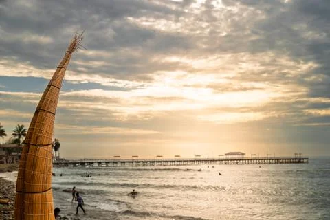 Traditional reed boat in sharp focus with blurred pier and sunset over Pacific O Stock-Fotos