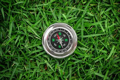 Traditional silver compass with red arrow on green grassy background Stock Photos